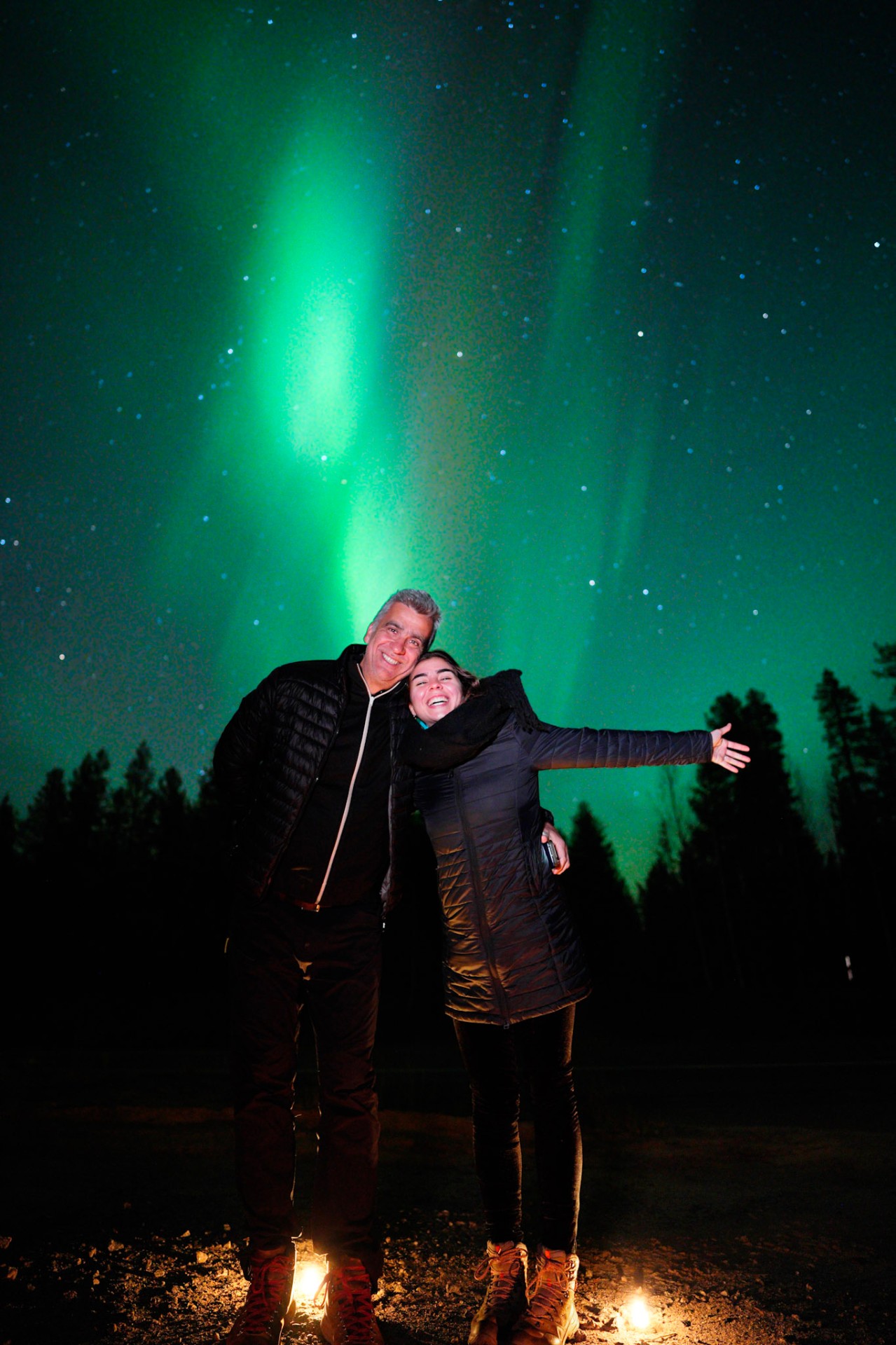 Couple cheering under a bright green aurora pillar in Rovaniemi