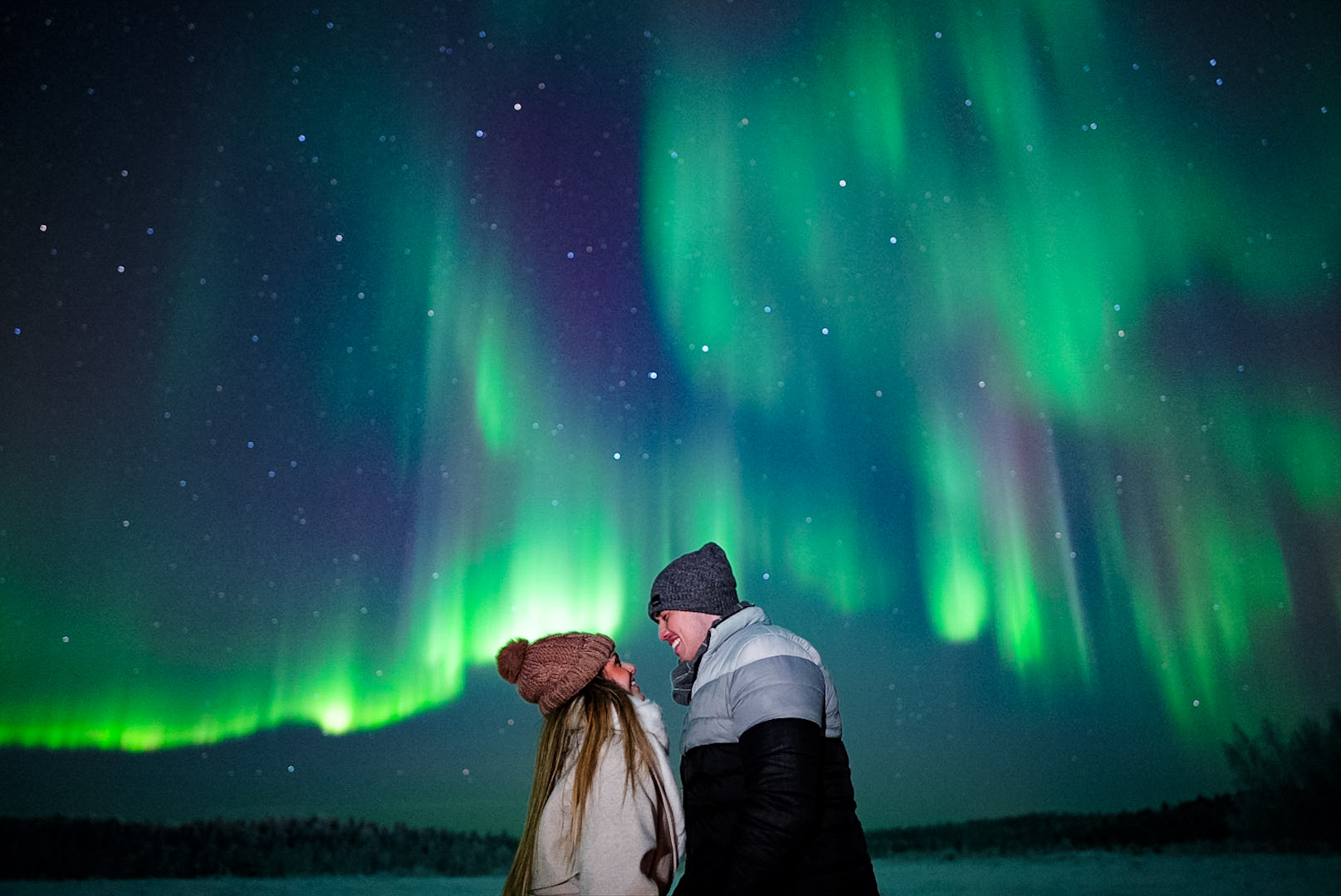 Couple holding hands under vibrant green northern lights in Finnish Lapland
