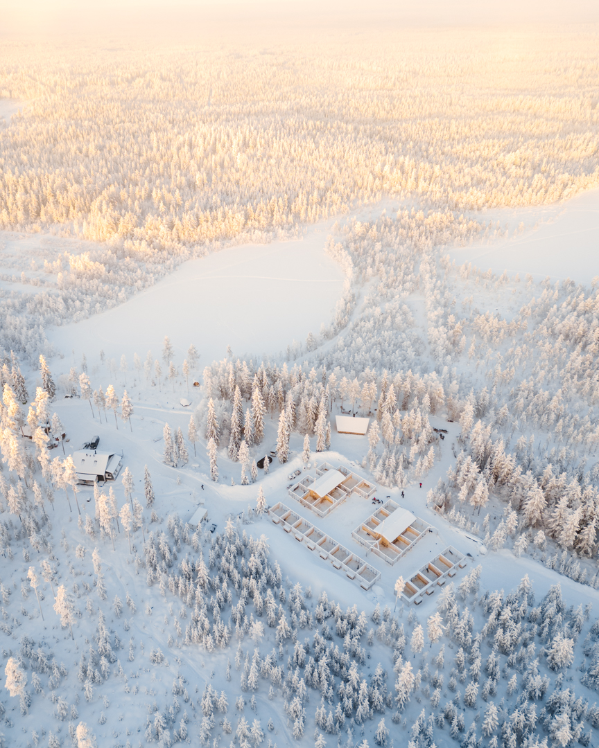 Aerial view of the husky farm surrounded by frosted forest at sunrise