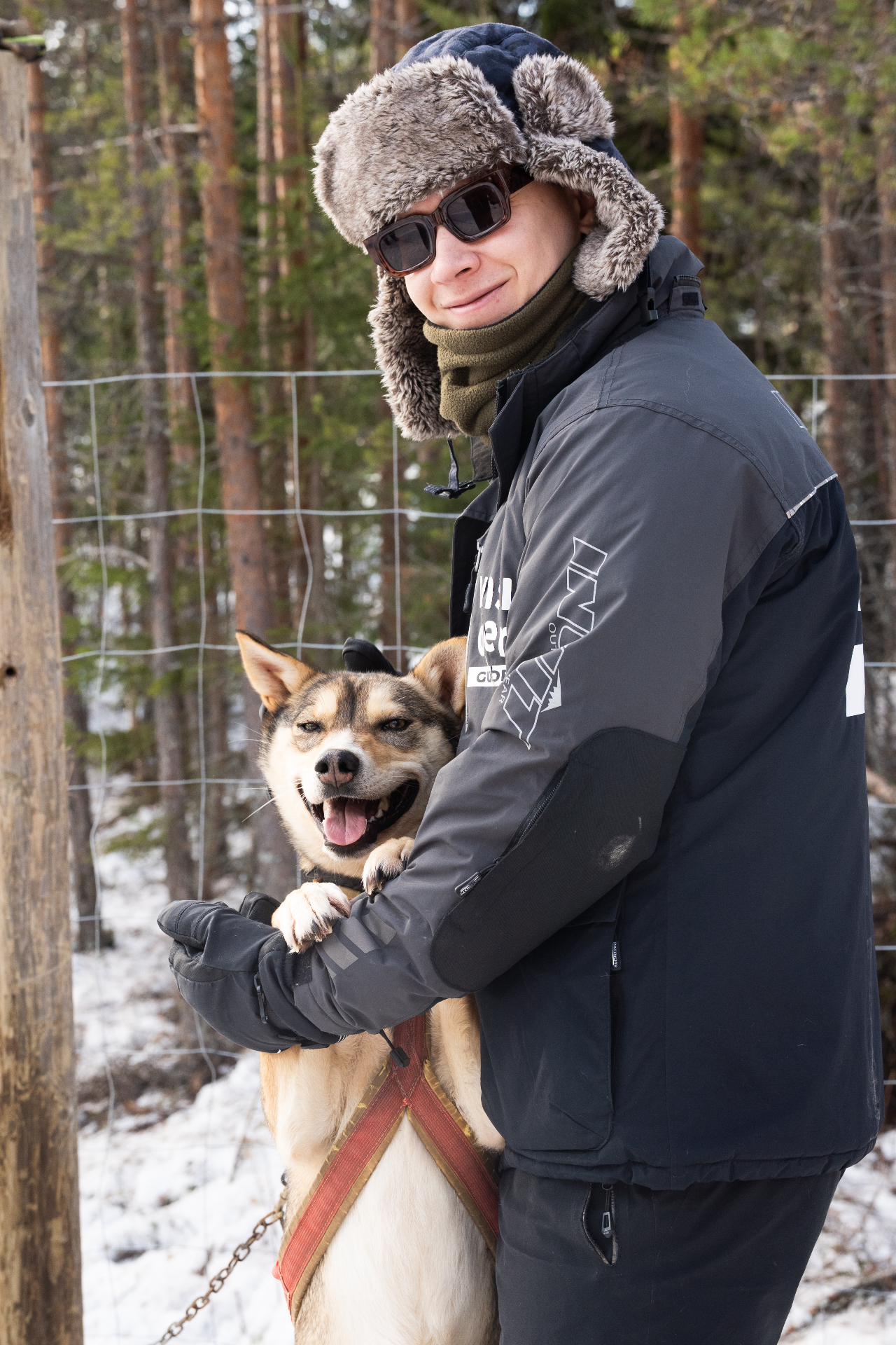 Musher hugging a smiling husky in the snowy forest