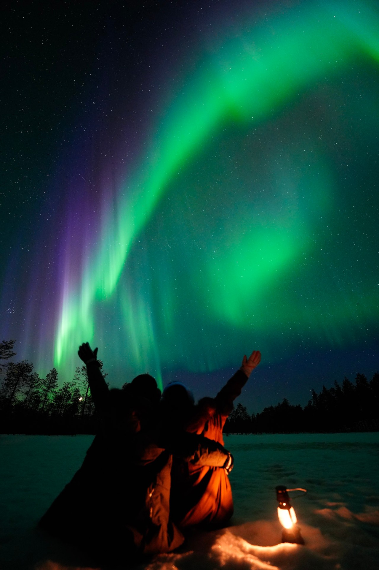 Friends reaching up under the aurora