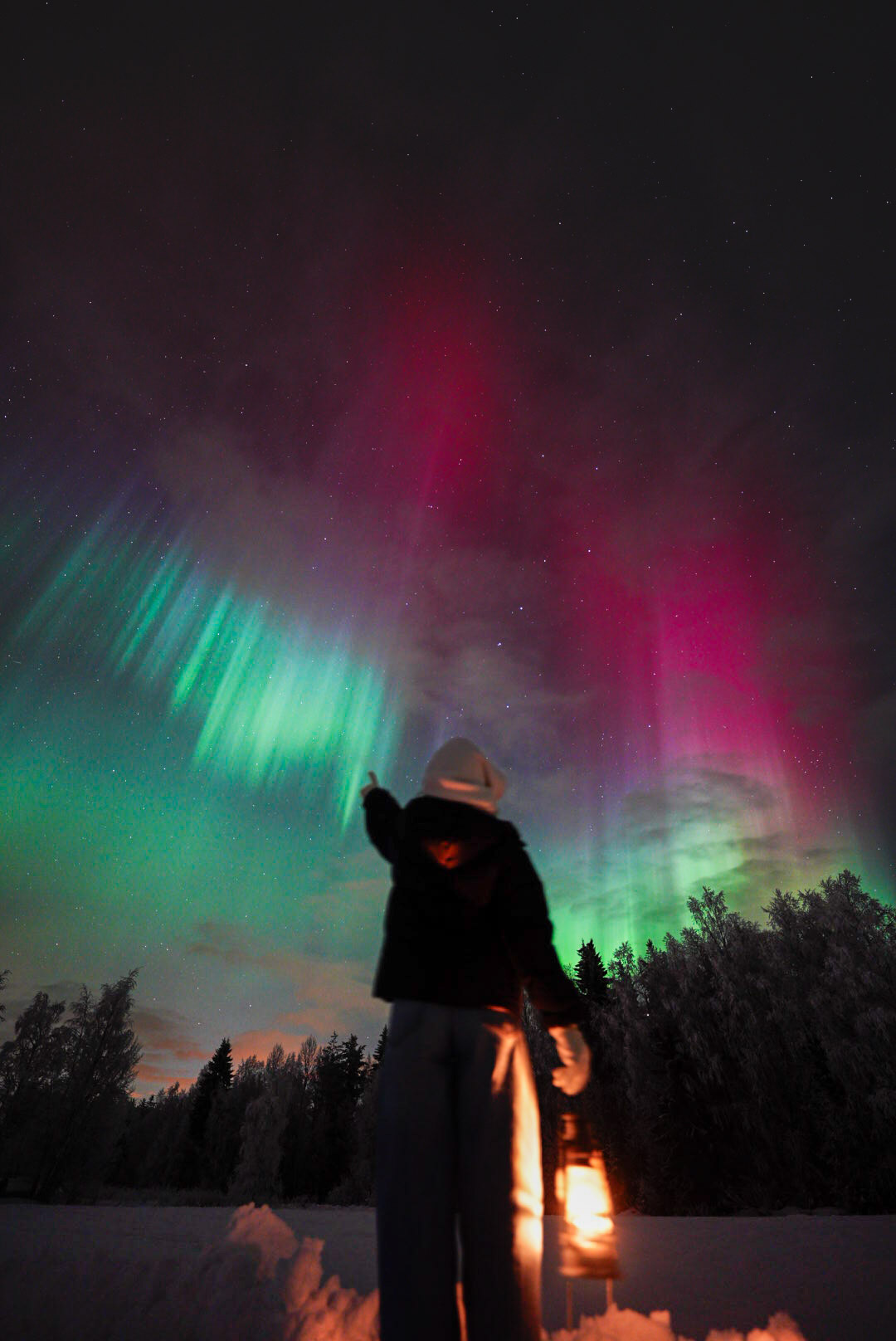 Guest with lantern under pink and green aurora