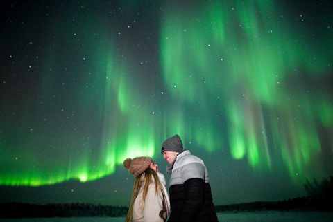 Couple smiling at each other under a green aurora curtain