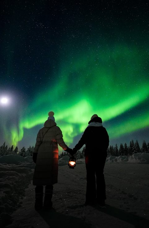 Couple holding hands with a lantern under the Northern Lights and the moon
