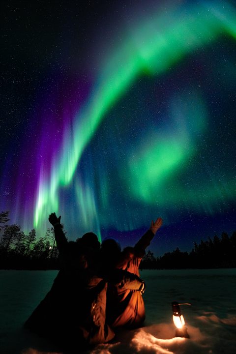 Gruppo di ospiti con lanterne che esulta sotto l'aurora