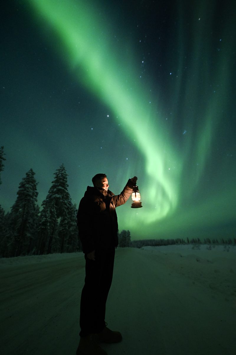 Ospite con una lanterna sotto un'aurora verde a notte fonda
