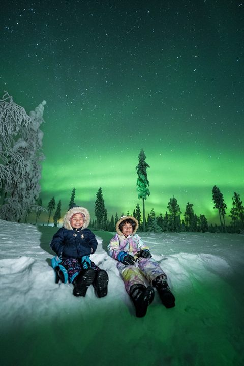 Two children sitting in the snow under the Northern Lights