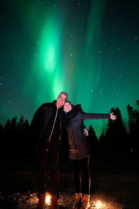 Paar jubelt unter einer hellgrünen Aurora-Säule in Rovaniemi