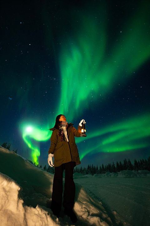 Gast mit Laterne unter einer weiten grünen Aurora in Finnisch-Lappland
