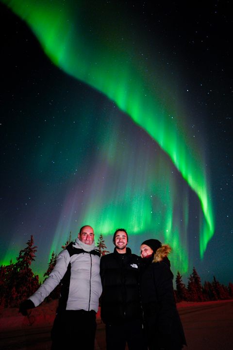 Familie unter einem leuchtend grünen Aurora-Band auf einer Polar-Lapland-Tour