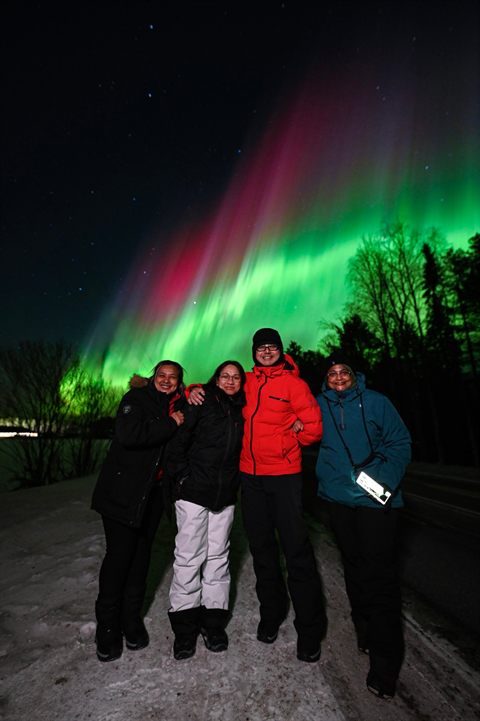 Gruppe von Freunden unter einer leuchtenden rot-grünen Aurora in Rovaniemi