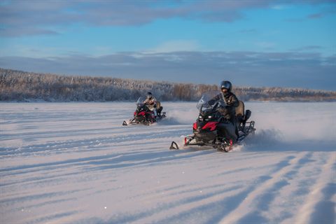 Zwei Schneemobile folgen der Strecke entlang eines vereisten Waldrands