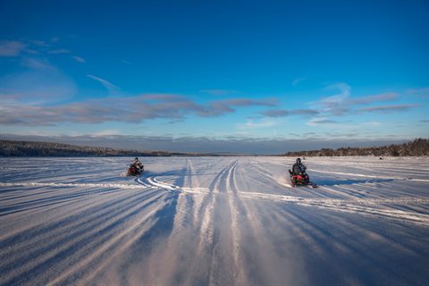 Schneemobilspuren ziehen sich über einen zugefrorenen See unter blauem Himmel